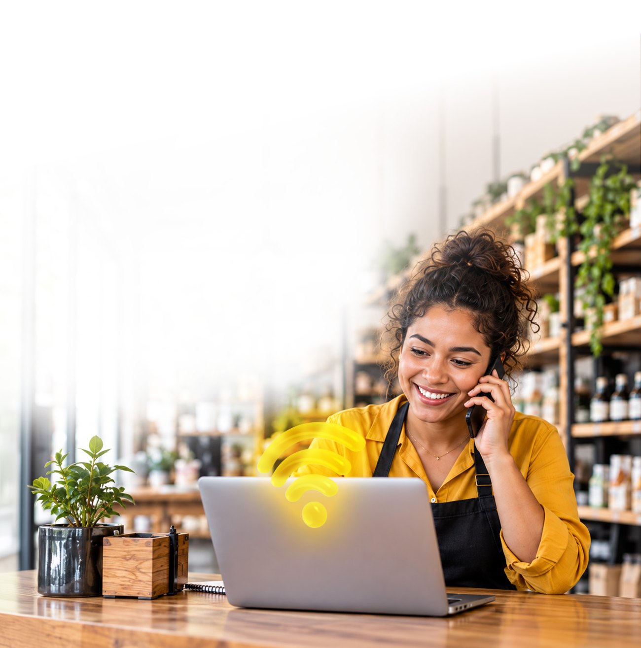Empreendedora em seu estabelecimento usando um notebook e falando ao telefone.